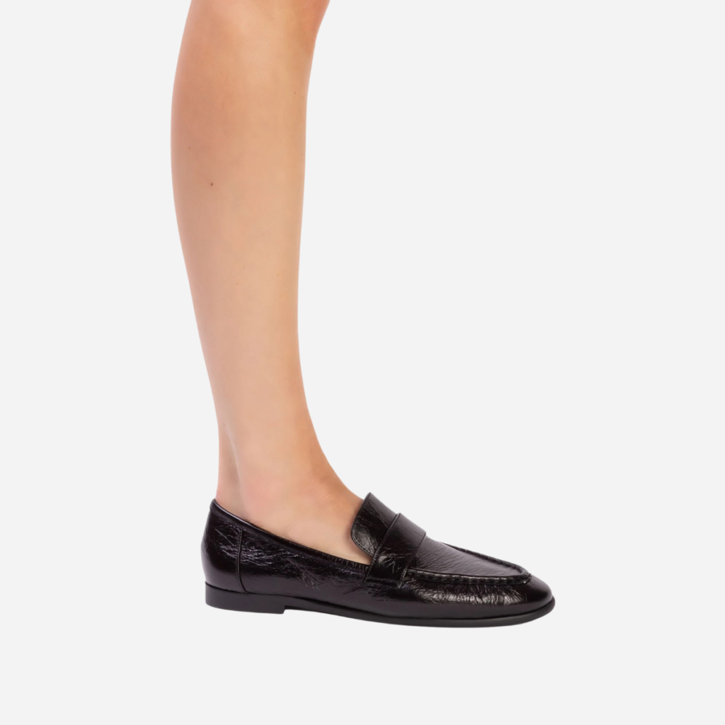 Black penny loafers by Black Suede Studio worn with bare legs, showing a relaxed everyday silhouette